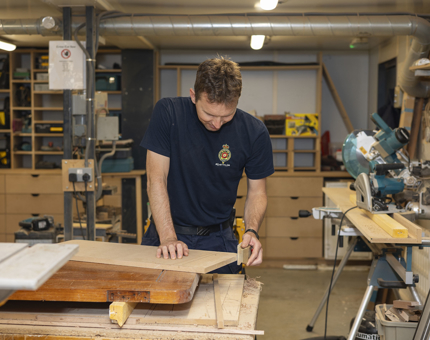A Maintenance team member sanding wood for a door in the workshop.