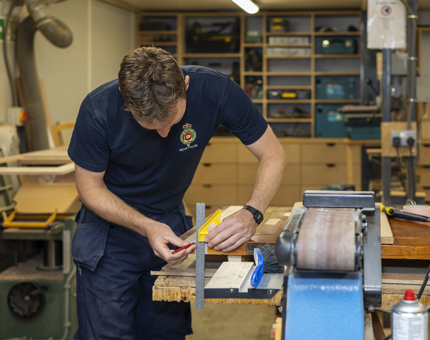 A Maintenance man measuring wood in the workshop.