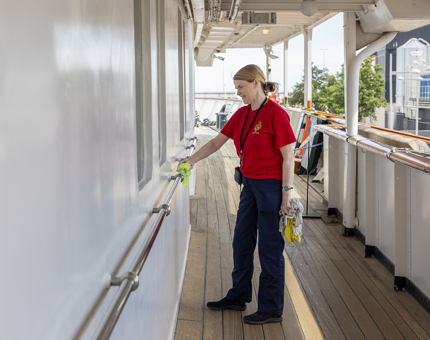 A Housekeeper is polishing a silver handrail that lines the deck of Britannia.