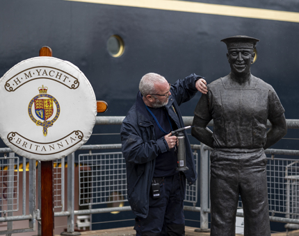 A Facilities Officer using a blow torch to remove oxidisation from a statue of an ex-yachtsman. 