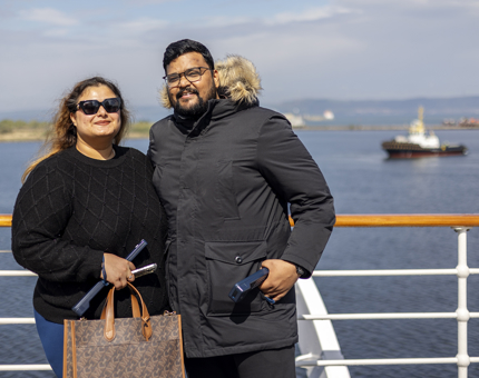 A man and a woman visitor standing in front of a railing with a waterfront view behind them.