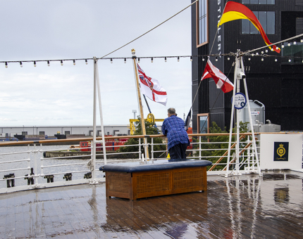 A rainy Verandah Deck where a visitor is leaning over the handrail and listening to their audio tour. 