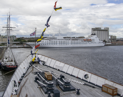 The bow of Britannia with a sailing ship and cruise liner in the background. 