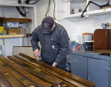A man in workshop varnishing wooden handrails.