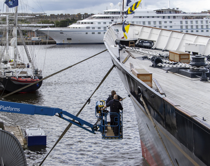 Two men in a cherry picker painting the hull of Britannia.