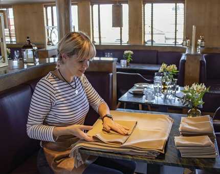 A Waiter sitting at a table in The Lighthouse Restaurant & Bar folding linen napkins.