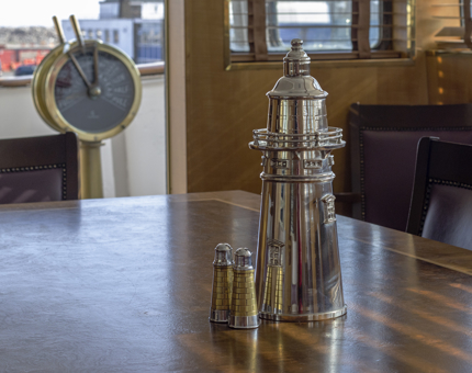Silver lighthouse salt and pepper cellars on a wooden table in Fingal's Bridge with the ship's engine order telegraph in the background. 
