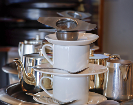 A tearoom tray piled with cups and saucers, silver teapots and milk jugs. 