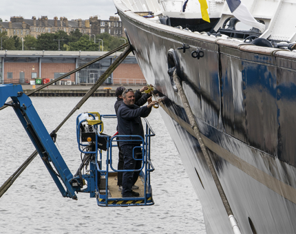 Two men from the Maintenance team use masking tape to prepare for the application of the gold leaf line. 