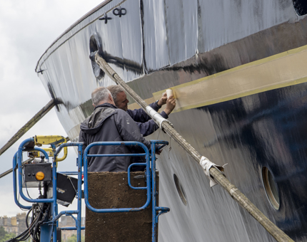 In a cherrypicker, two men apply the gold leaf to the side of Britannia.