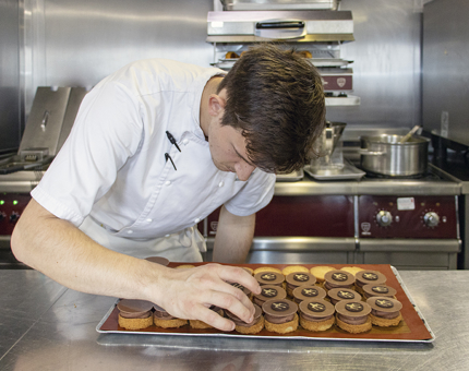 A Chef adds chocolate discs to the top of millionaire shortbread in the Galley.