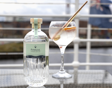 A bottle of Fingal gin with a gin and tonic in a glass outside on the deck.