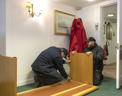 Two members of the Maintenance team assembling a wooden desk in an office.