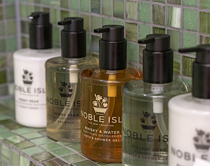 Five bottles of Noble Isle products including shower gels and lotions on a shelf in a bathroom at Fingal. 