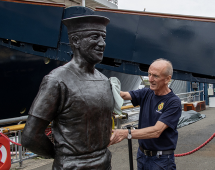 A man from the Facilities Team wipes down the bronze statue of a former Royal Yachtsmen. 