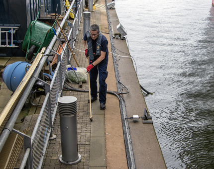 A man wearing a lifejacket is sweeping on the Quayside. 