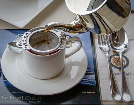 A silver teapot is pouring loose leaf tea into a teacup.