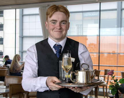 A Waiter holding a tray in the Tearoom containing a teapot and other drinks.