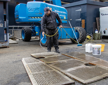 A man hoses down wooden deck plates on the ground next to a cherrypicker. 