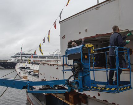 Two members of the Maintenance team on a cherrypicker apply filler to the bulwark.