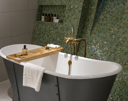 A luxurious bathroom with roll top bath and green mosaic tiled wall. 