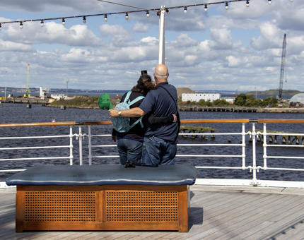 A man and a woman couple pose for a selfie photograph on Britannia's Verandah Deck. Their backs are to the camera.