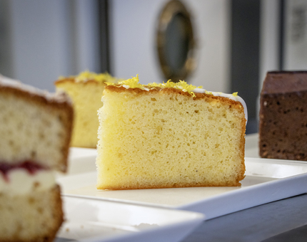 Slices of freshly baked cakes including lemon drizzle, Victoria sponge and chocolate fudge cake on plates.