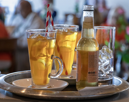 Tall glasses of iced tea and a bottle of ginger beer on a tray. 