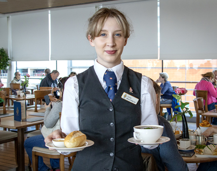 A Waiter in the Royal Deck Tearoom carries a cup and saucer and a bowl of soup.