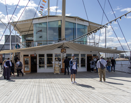 The outside of the Sun Lounge and the Royal Deck Tearoom above from the Verandah Deck. There are several visitors on the deck listening to audio guides. 