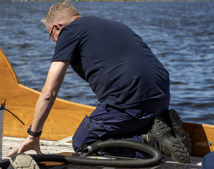 A man using a tool to remove the caulking on the yacht, Bloodhound. 