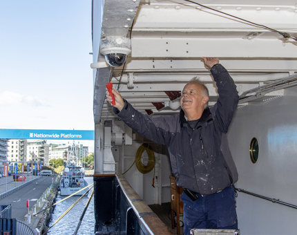 A man reaching up to paint the underside of a deck. 