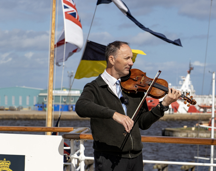 A man playing the violin on the outside deck. 