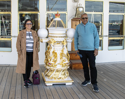 A woman and a man standing next to The Royal Yacht Britannia's binnacle compass. 