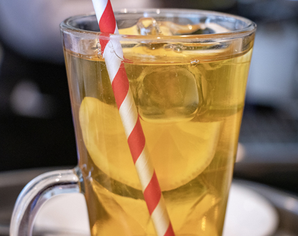 A close-up of a glass of iced tea with a red and white striped straw.