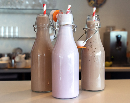 Two chocolate and one strawberry milkshakes in milk bottle glasses with straws. 