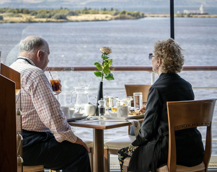 A couple eating lunch at a table overlooking the water in the Royal Deck Tearoom. 
