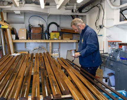 A man varnishing wooden handrails in the Maintenance workshop.