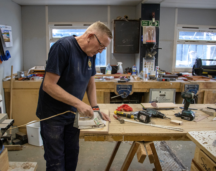 A man uses an iron in the workshop to remove scratches on a cupboard door. 
