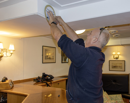 A member of the Maintenance Team putting up a tour route sign for visitors in the Wardroom. 