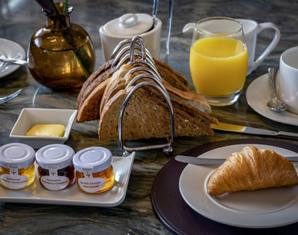 A Fingal breakfast comprising of croissant, rack of toast, preserves, butter and a teacup and saucer.