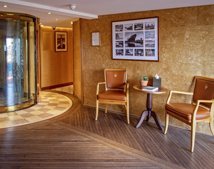 Fingal Hotel's Reception with the a lift, two leather backed chairs and a coffee table. Black and white photographs of lighthouses are on the wall. 