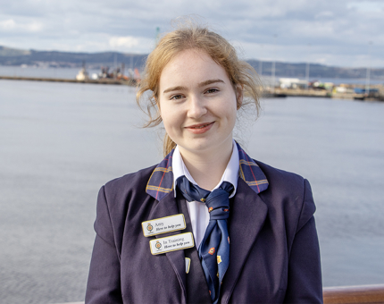 A smiling woman in Britannia uniform standing with a background of water.