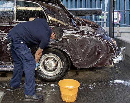 A man washing a maroon Rolls Royce car with a sponge and bucket.