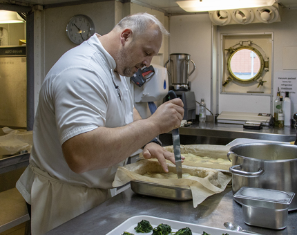 A Chef using a knife to prepare a dish in the Galley. 