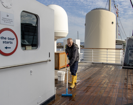 A member of the Maintenance team scrubbing the deck next to the Bridge on the Flag Deck.