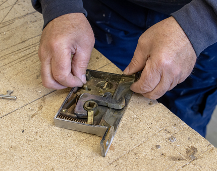 A close-up of a man fixing a door lock mechanism on a workbench.