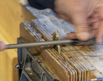 A close-up of a part of a doorlock being worked on in a vice. 