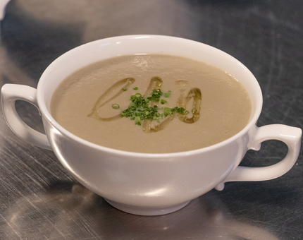 A two-handled bowl containing mushroom soup with garnish. 