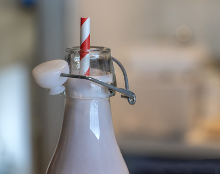 A close-up of a strawberry milkshake with red and white striped straw in the top of the bottle. 